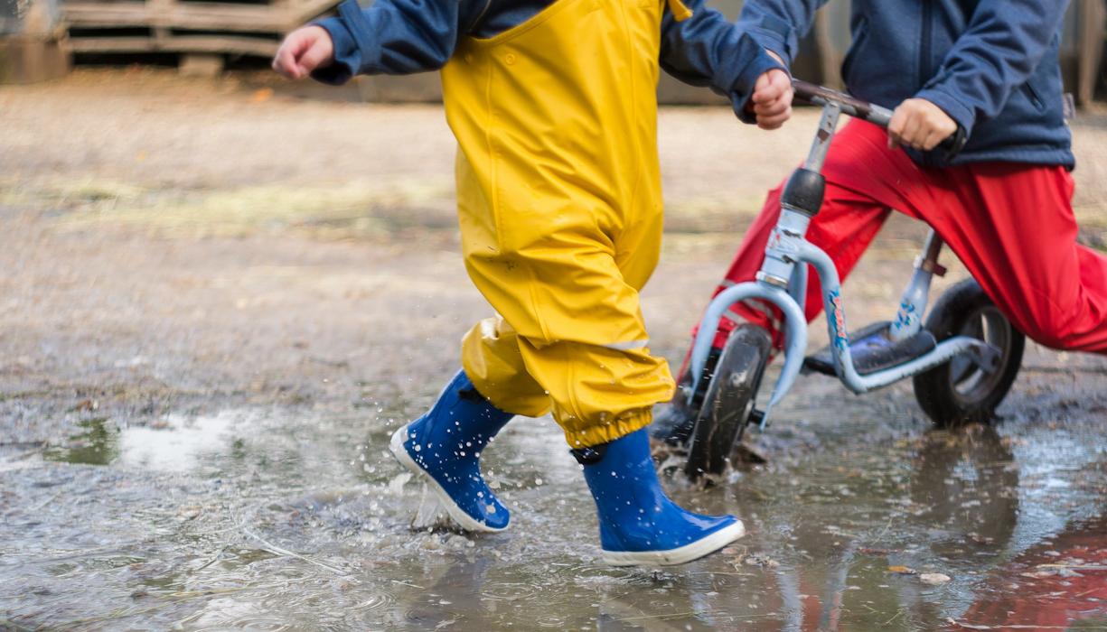 Spielende Kindergartenkinder in Pfütze mit Roller und Gummistiefel