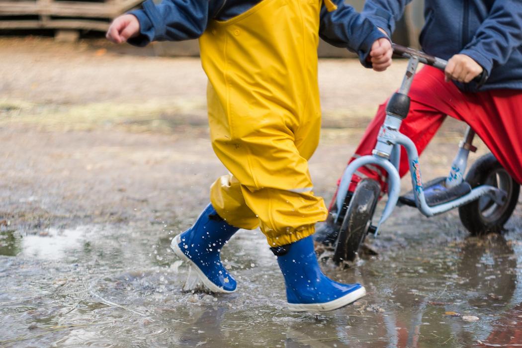 Spielende Kindergartenkinder in Pfütze mit Roller und Gummistiefel