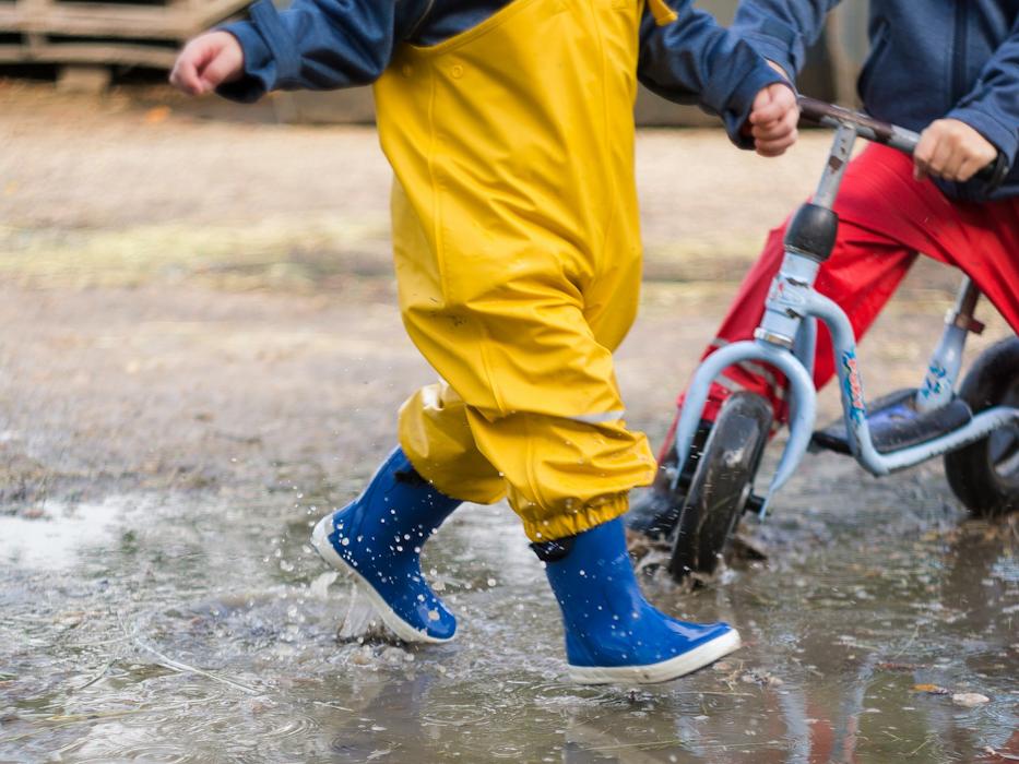 Spielende Kindergartenkinder in Pfütze mit Roller und Gummistiefel